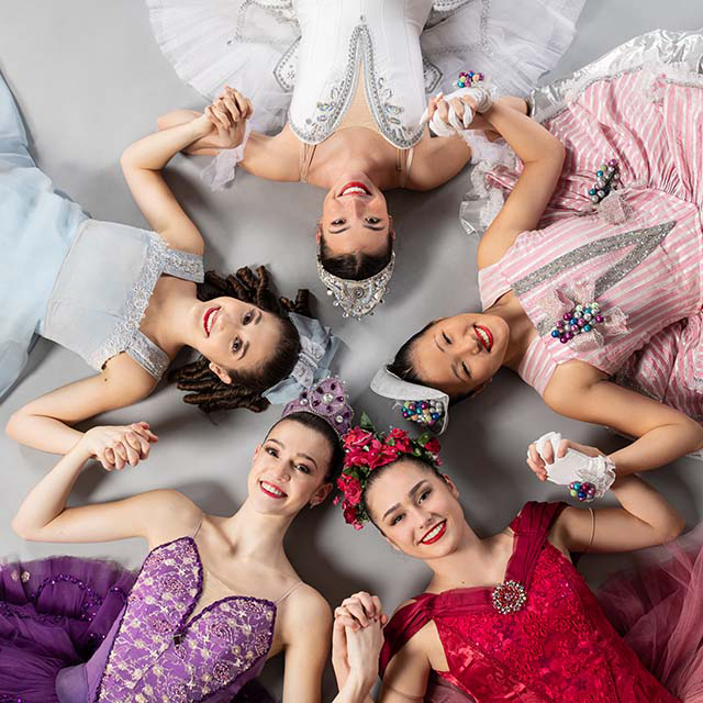 Group of female Nutcracker character dancers laying on floor in a circle with heads together and holding hands